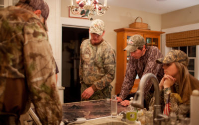 Image de plusieurs personnes en tenue de camouflage à l'intérieur d'une maison se préparant à partir à la chasse.
