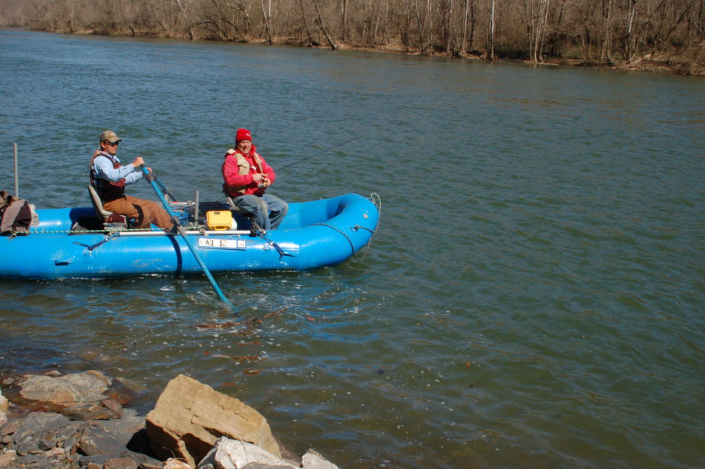 Image de deux hommes sur un radeau bleu pêchant près d'un bassin rocheux profond.