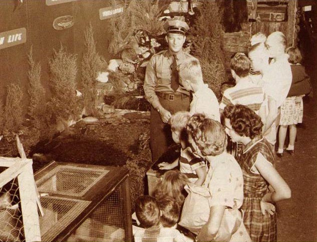 Image en noir et blanc d'un garde-chasse s'adressant à des enfants.