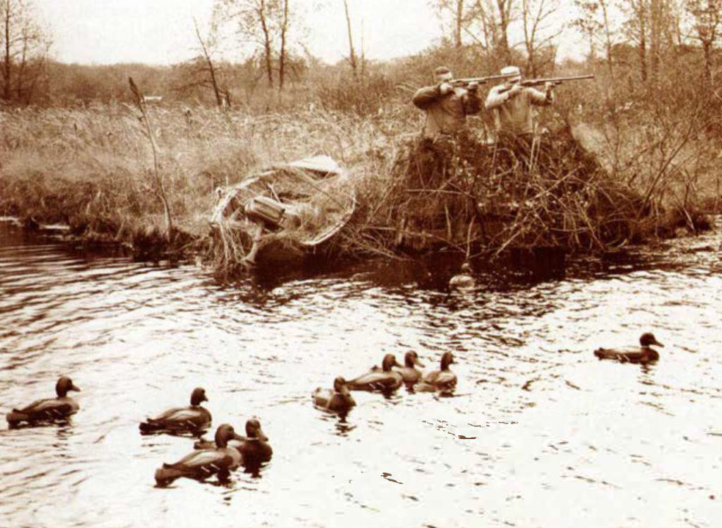 Image de deux chasseurs devant une rivière remplie de gibier d'eau.