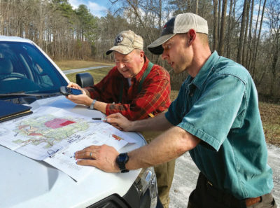 Image de deux hommes regardant une carte placée sur le capot d'un camion blanc alors qu'ils décident de l'emplacement de leurs nichoirs.