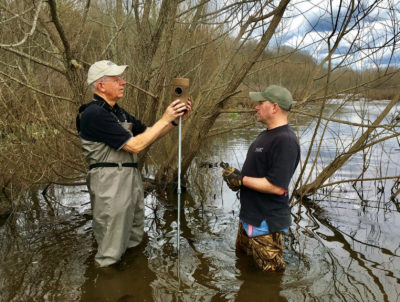 Image de deux employés de la centrale électrique de Trèfle plaçant un nichoir sur un support dans une rivière.