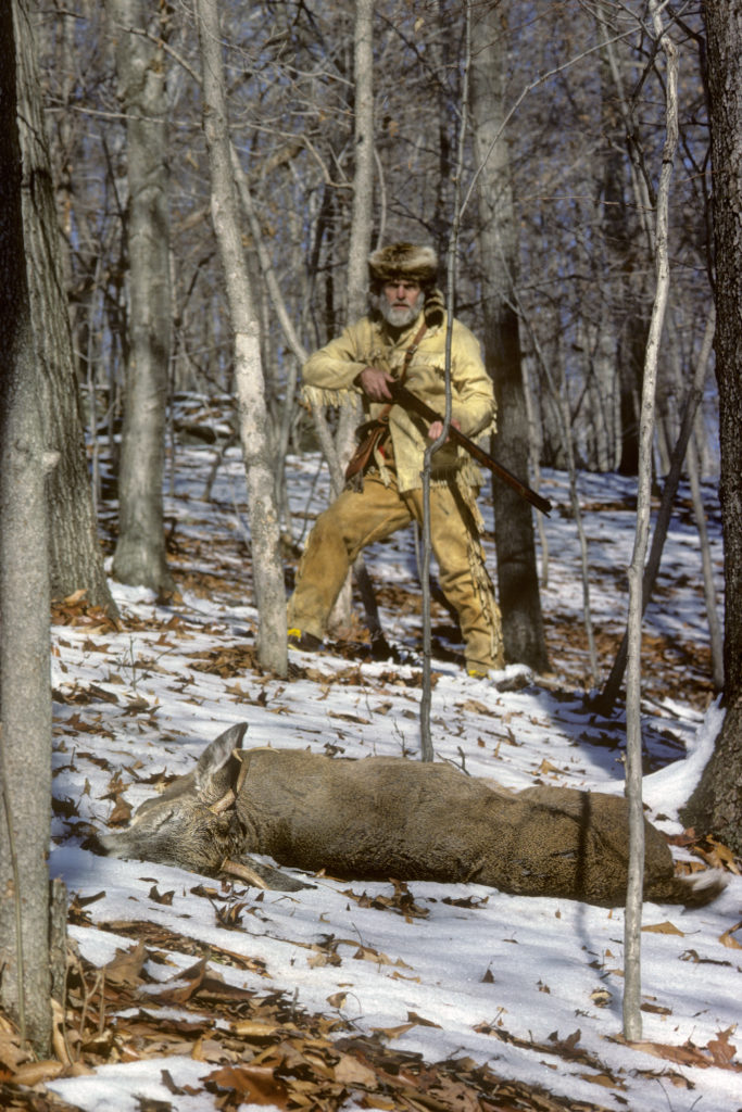 Image d'un chasseur avec un cerf mort devant lui, qu'il a abattu avec un fusil à chargement par la bouche.
