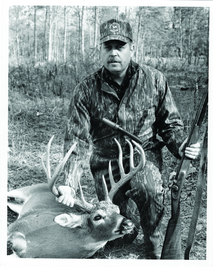 Photo en noir et blanc d'un homme, d'un cerf et d'un fusil à chargement par la bouche.