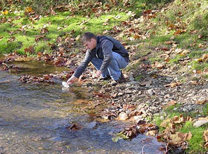 Image d'un biologiste debout sur un rivage, utilisant un gobelet pour prélever un échantillon d'eau.