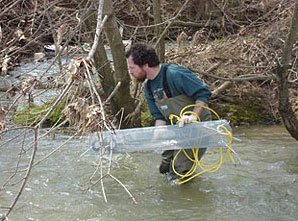 Image d'un biologiste plaçant dans l'eau une grande structure métallique connue sous le nom d'échantillonneur chimique passif.