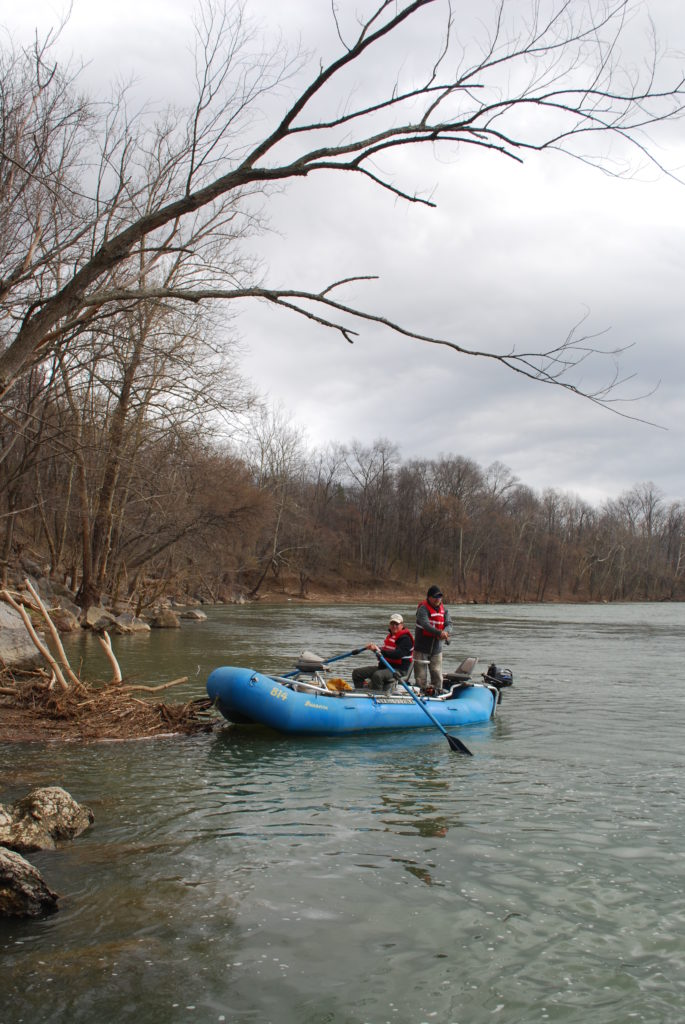 Image de deux personnes pêchant dans des gilets de sauvetage rouges sur un radeau bleu à New River ; il est important de voyager avec un ami en plein air, en particulier lorsque les conditions météorologiques ou les températures sont dangereuses.