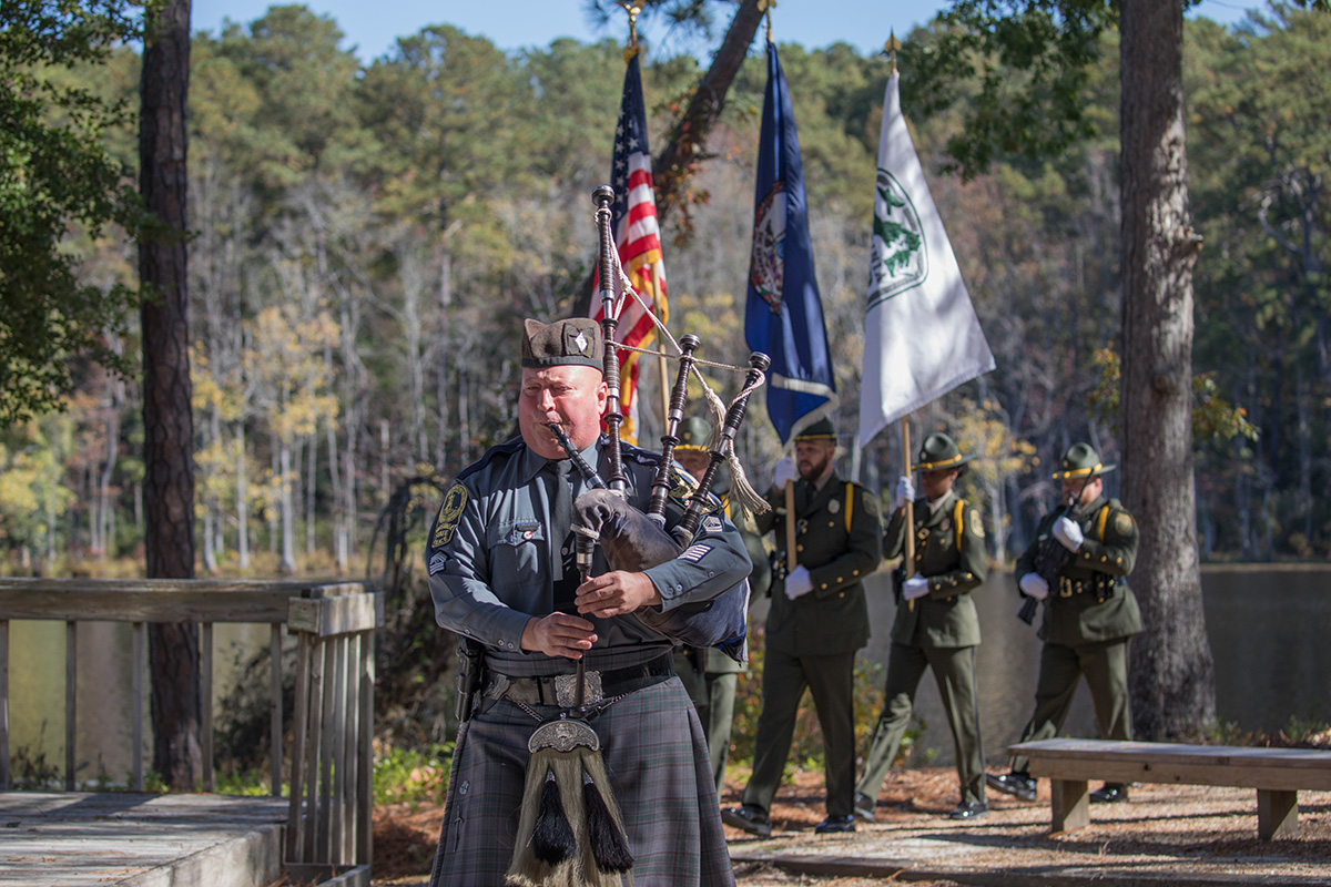 Image d'un homme avec une cornemuse dirigeant une cérémonie d'inauguration de la garde d'honneur du DWR dans une forêt de feuillus.