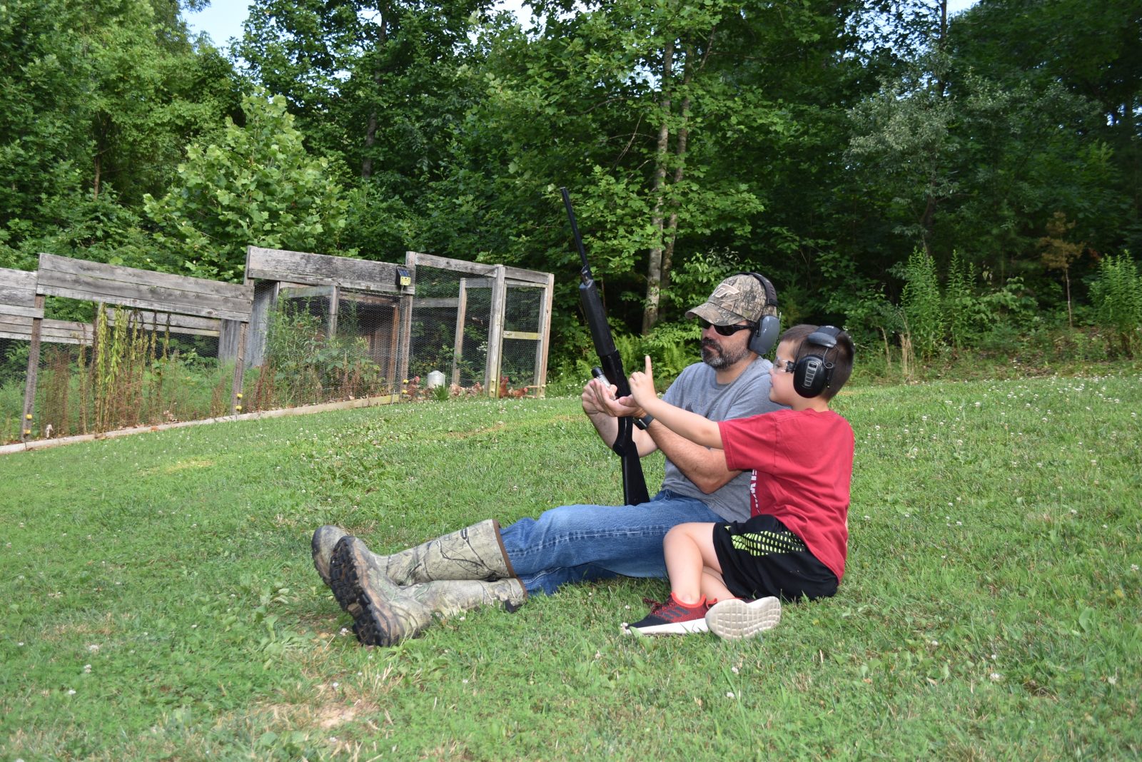 L'image d'un jeune enfant et de son père assis dans une prairie avec une arme à feu, faisant le point sur la sécurité des armes à feu.