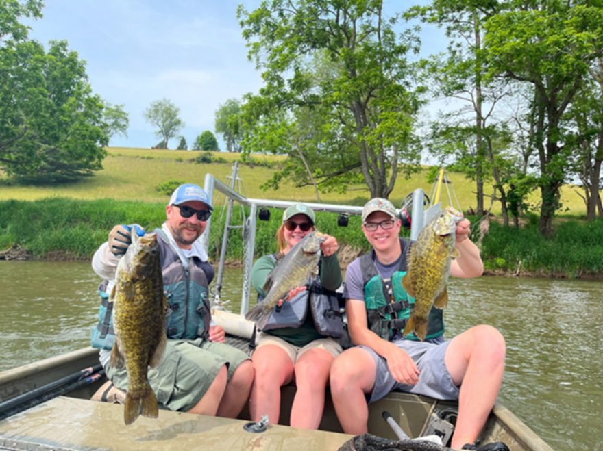Trois pêcheurs assis sur un bateau transportant des poissons sur la haute rivière New River.