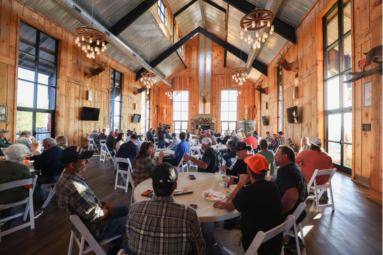 Un grand groupe de personnes réunies autour de tables pour un repas dans un grand bâtiment ouvert.