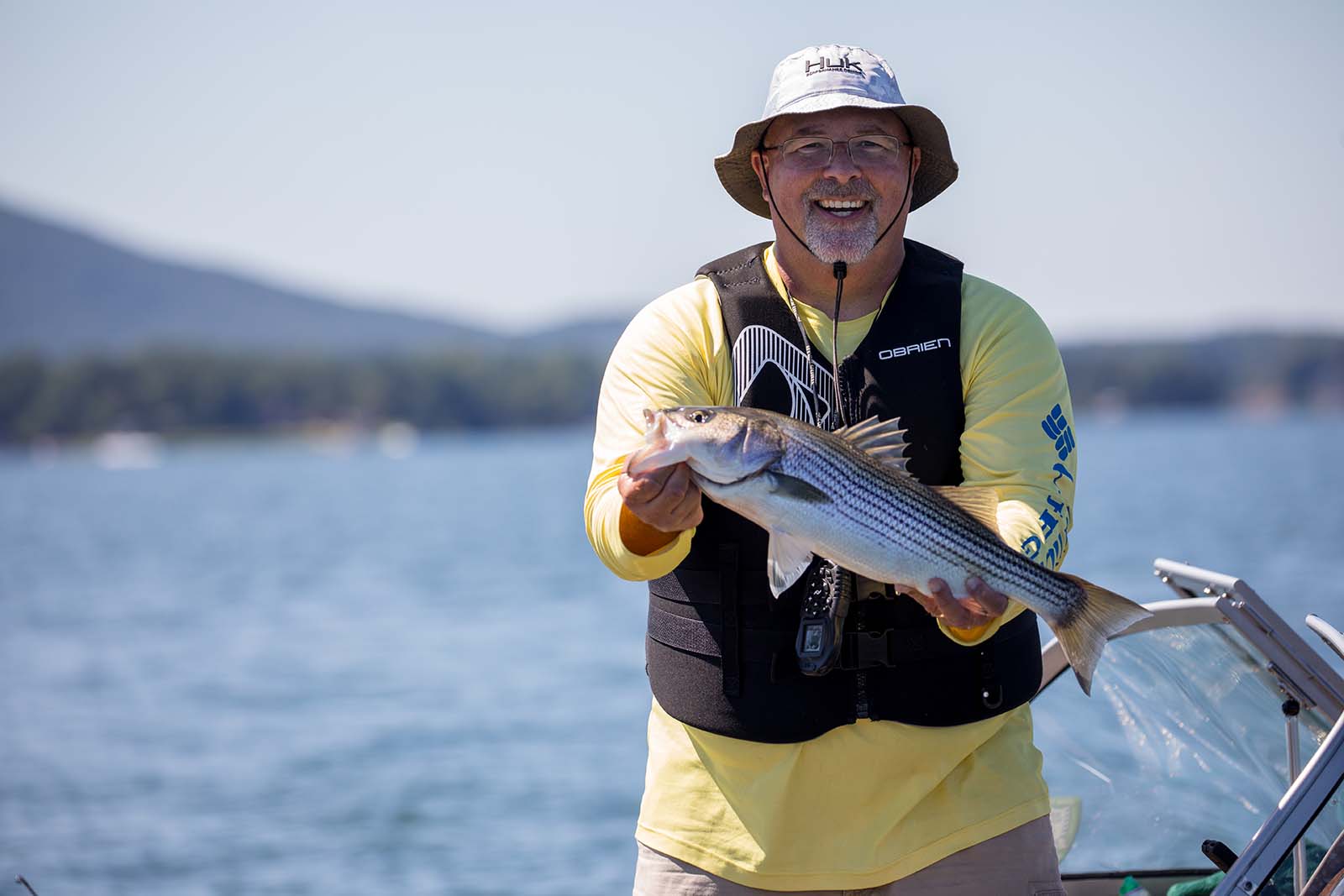 Un homme portant un chapeau à godets et un gilet de sauvetage sourit à l'appareil photo tout en tenant un poisson.