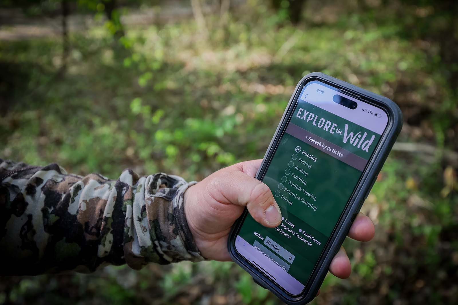 Une main tenant un smartphone avec Explore the Wild affiché