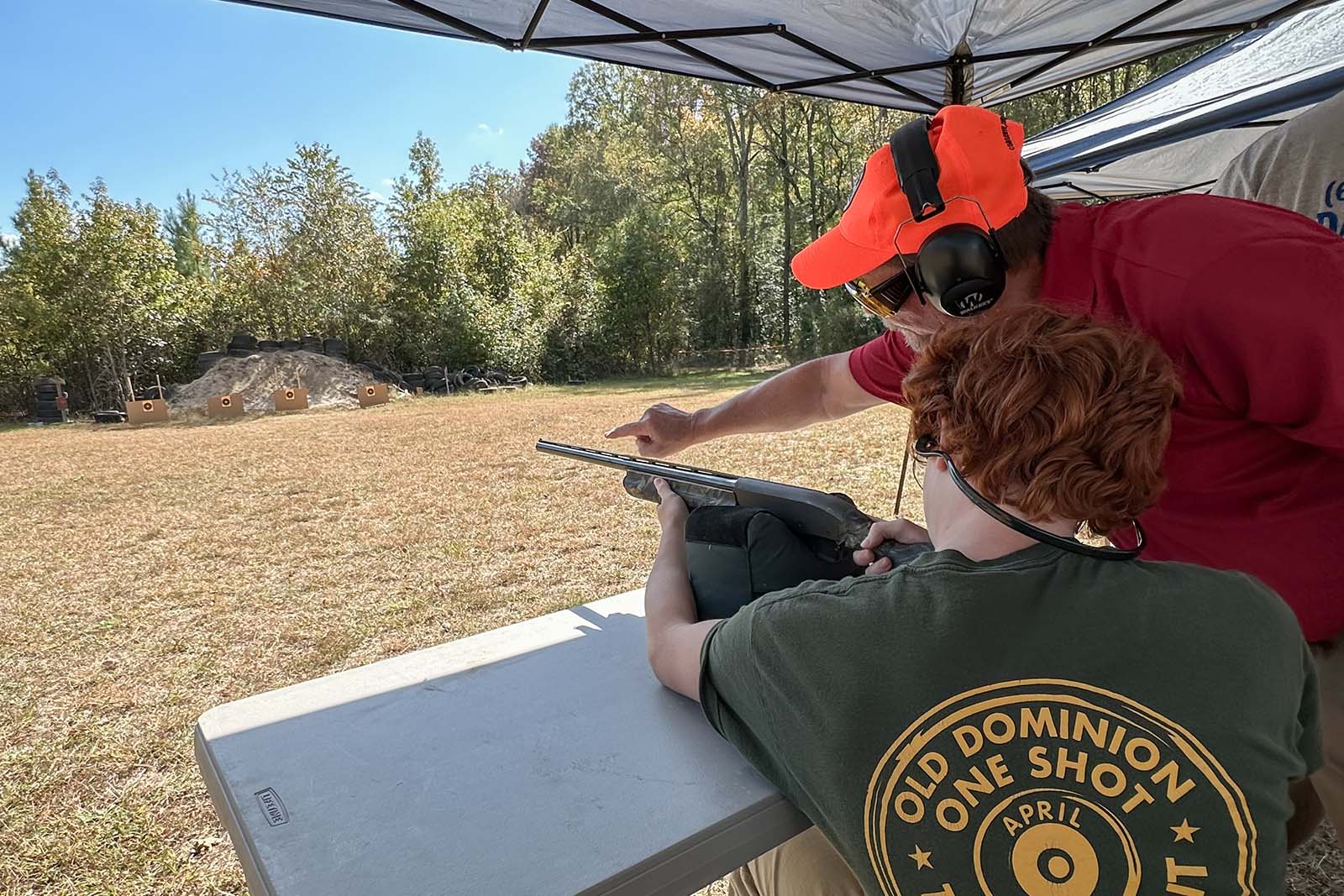 Une personne s'entraîne à tirer sur des cibles avec un fusil de chasse ; un instructeur se tient à proximité et pointe la cible.