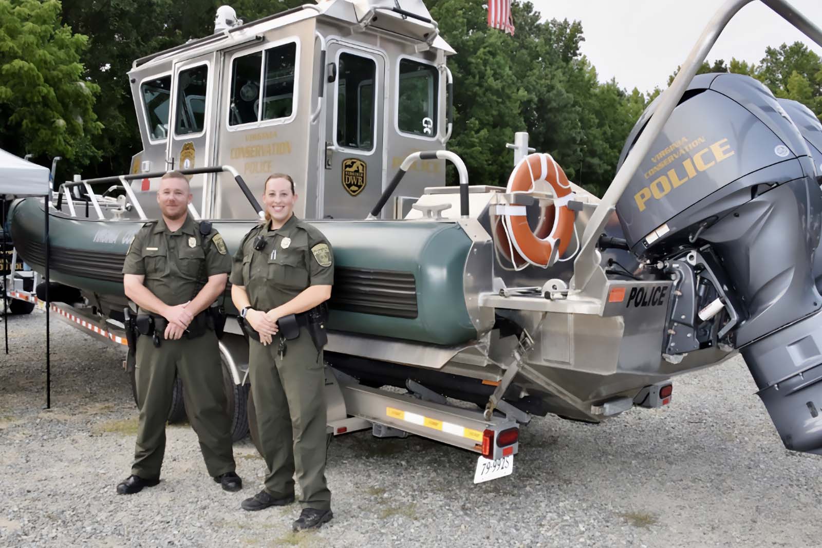 Des agents de police se tiennent devant un bateau de police monté sur une remorque.