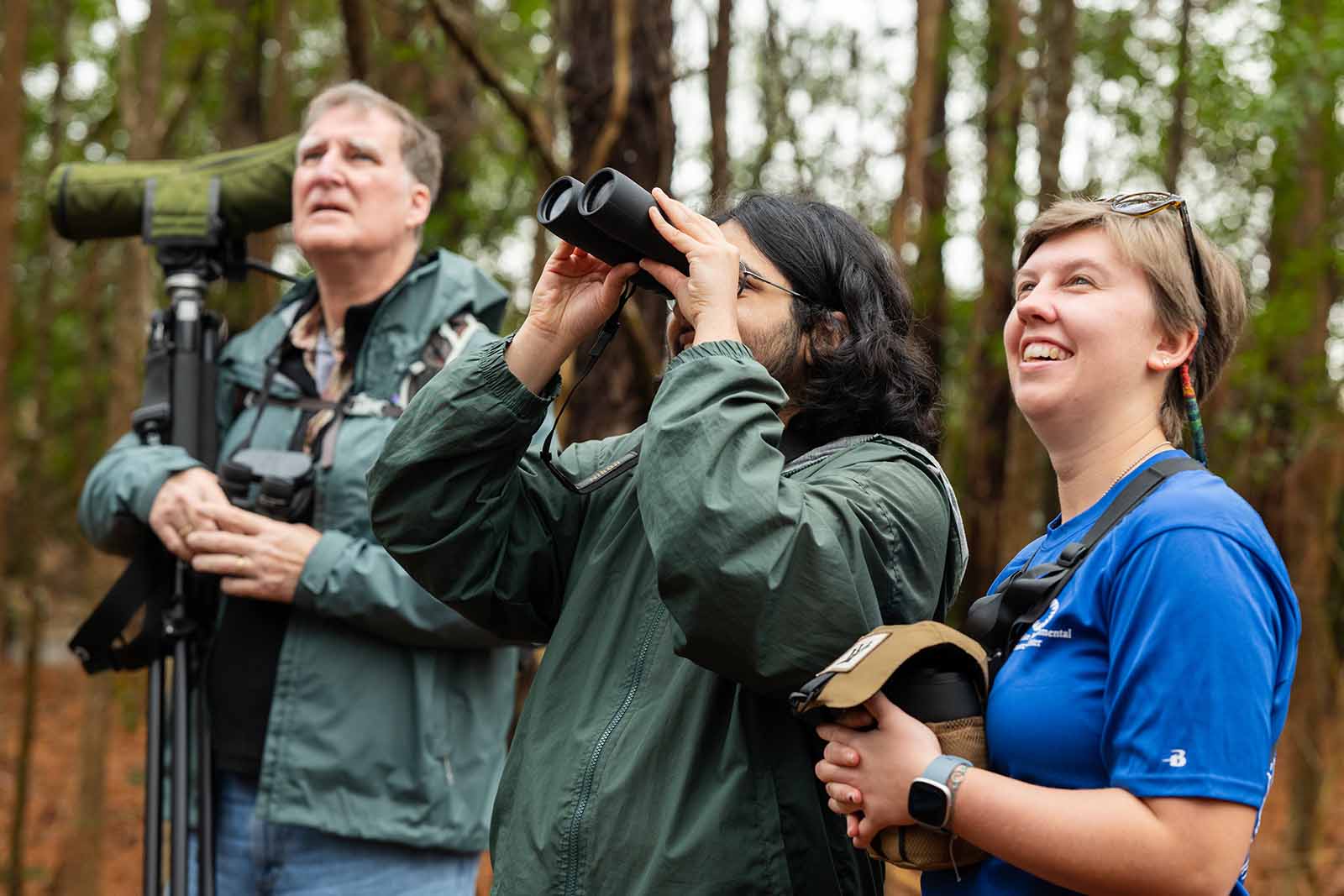 Deux personnes en veste vert foncé regardant vers le haut, l'une utilisant une paire de jumelles