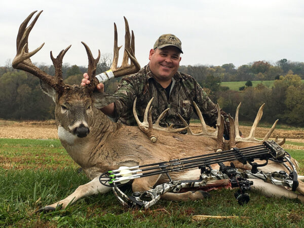Image d'un chasseur à côté d'un cerf mâle qu'il a tué à l'aide d'un arc et de flèches.