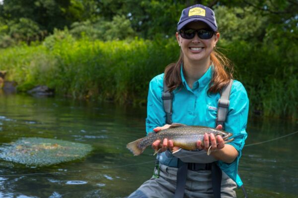 Femme en tenue de pêche, souriante et tenant un omble de fontaine pour la photo.