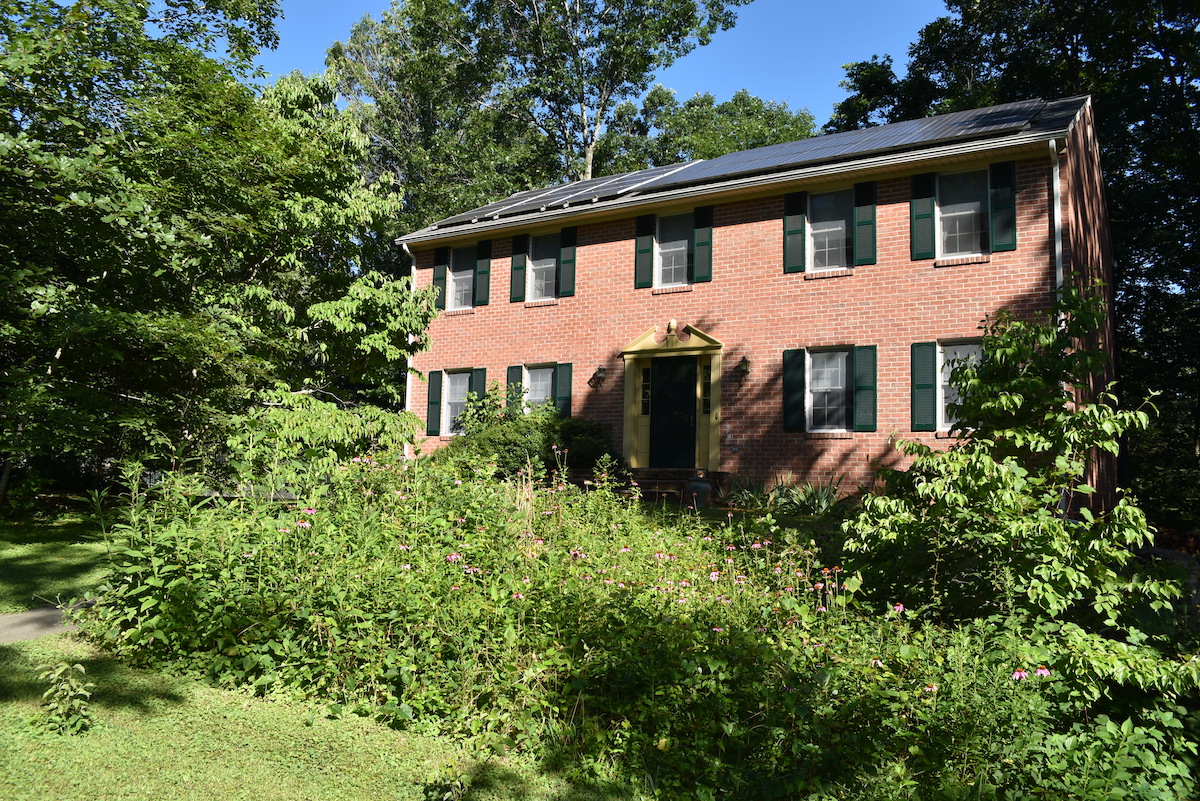 Image d'une maison en briques avec des panneaux solaires sur le toit et un jardin de pollinisateurs dans la cour avant.