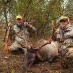 Deux hommes posant avec un élan mort, tenant sa tête par les bois.