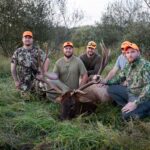 Cinq hommes posant avec un élan mort, entouré d'arbres clairsemés.