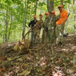 Cinq hommes posant avec un élan mort, entouré d'une forêt.