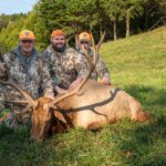 Trois hommes posant à genoux devant un élan mort.