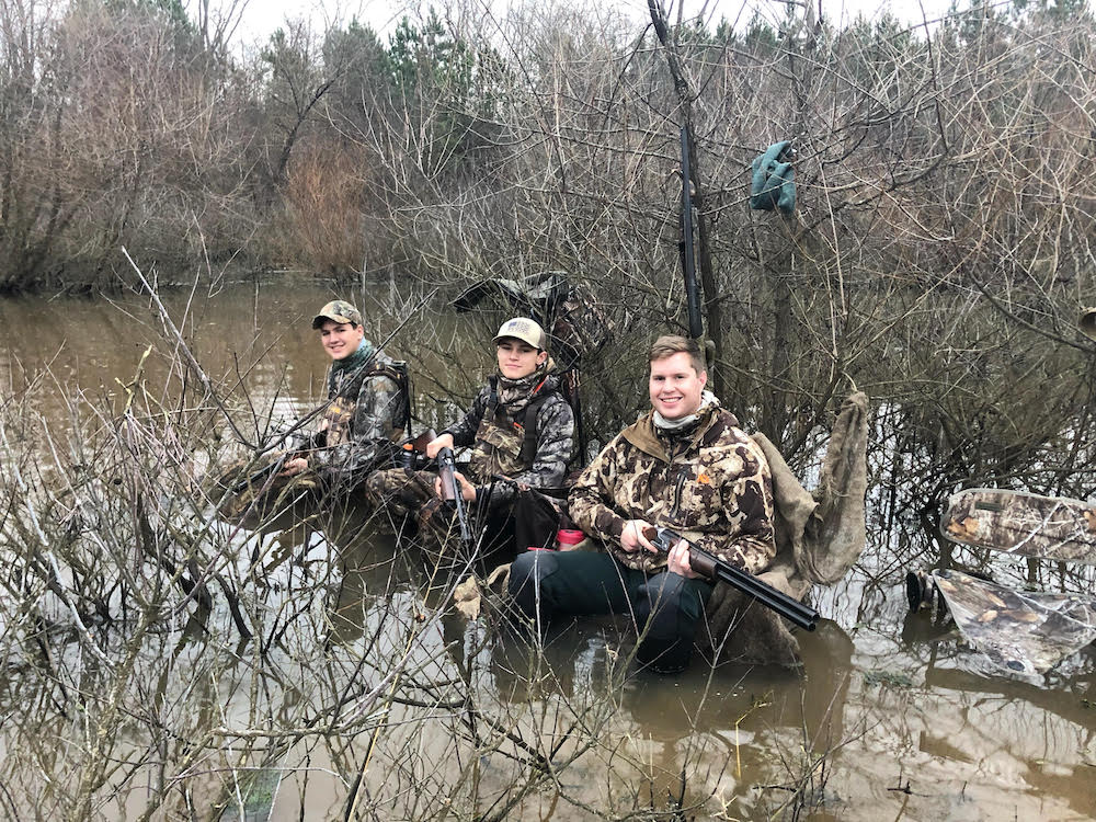 Image d'un groupe d'hommes assis sur un rondin dans l'eau, ils n'ont pas trouvé de canard cette fois-ci.