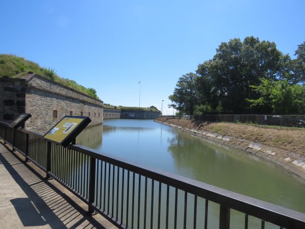 Image d'une douve à l'intérieur du fort Monroe avec une falaise escarpée et fenêtrée d'un côté et un champ d'herbe beaucoup plus lisse de l'autre ; cette image a été prise au centre d'accueil des visiteurs.