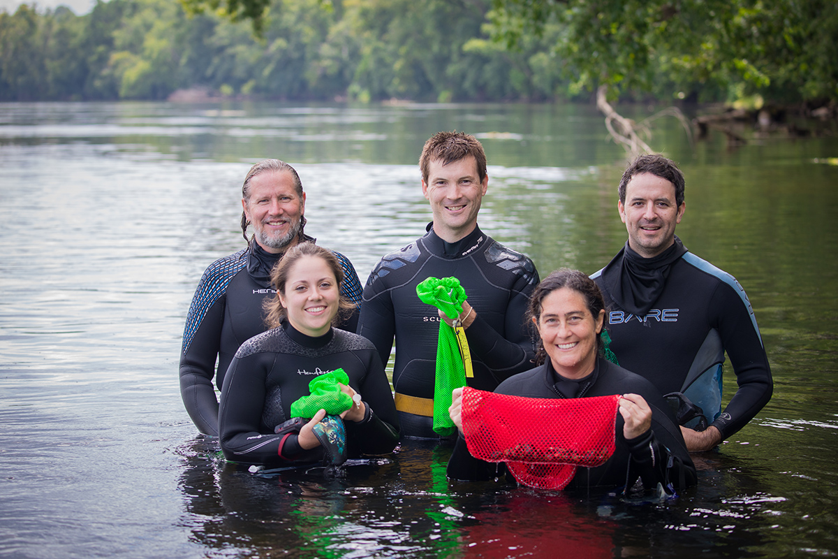 Image de cinq personnes posant pour une photo dans une rivière ; elles tiennent des sacs de moules.