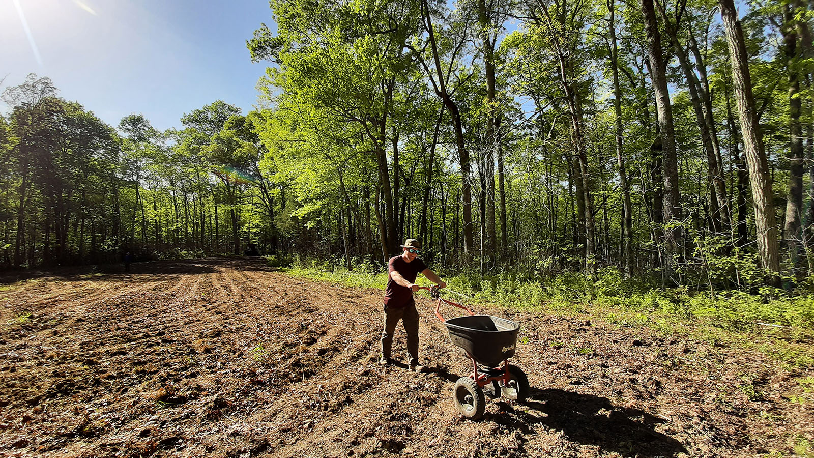 Image d'un homme préparant un champ pour la restauration d'une prairie ; il est en train de répandre des graines sur le sol retourné.