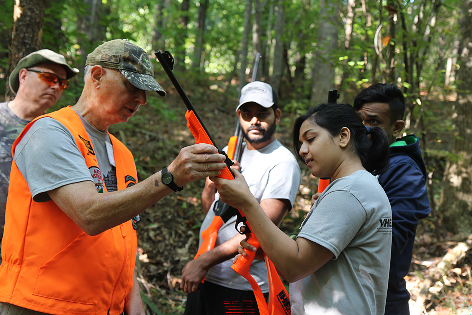 Photo d'un homme expliquant à une femme comment tenir un fusil de chasse sous le regard d'un groupe.