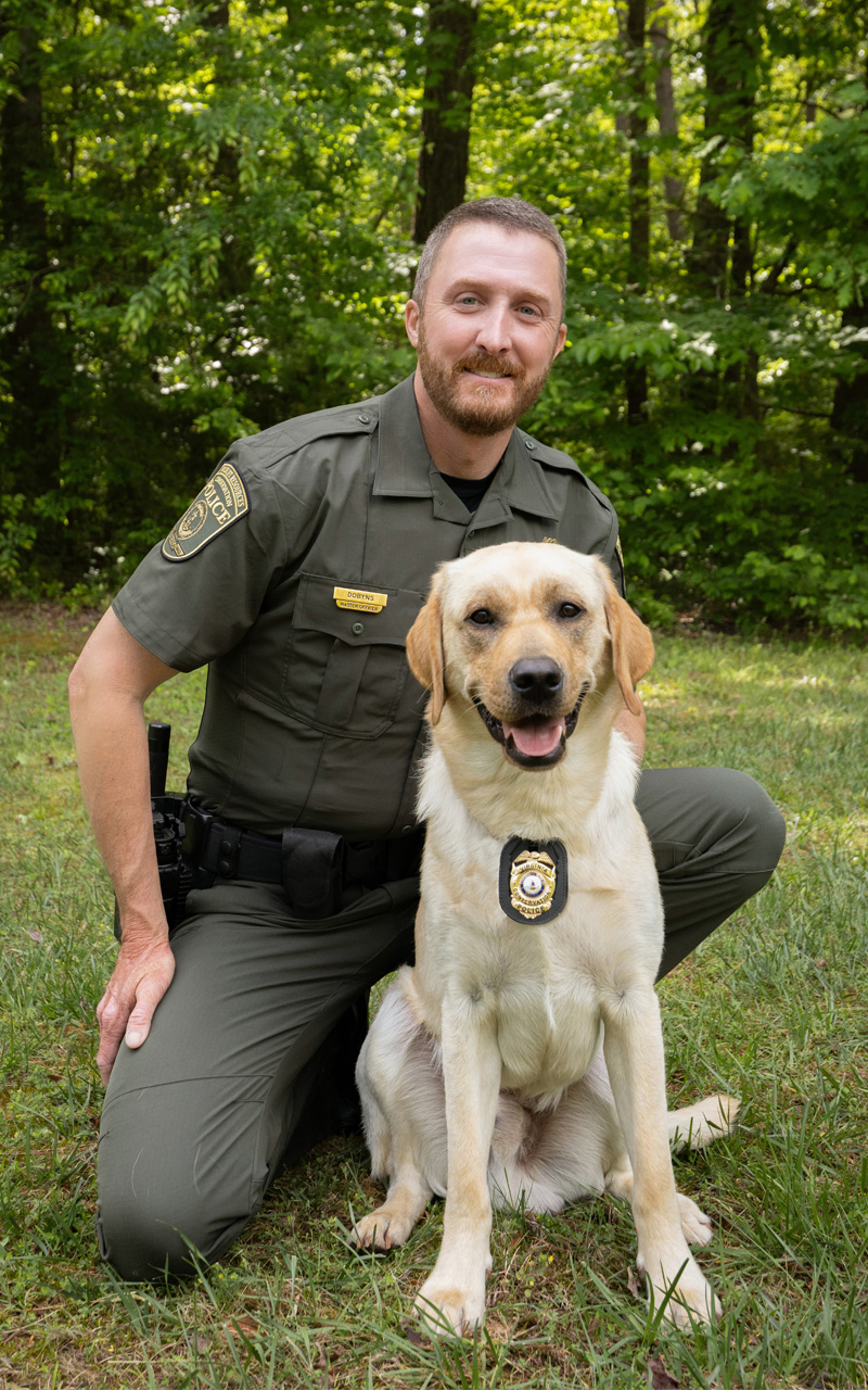 La photo d'un agent des forces de l'ordre en uniforme agenouillé à côté d'un chien portant un insigne au collier.