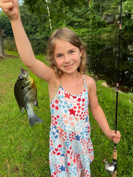 Une jeune fille, âgée de 6, tenant un poisson sur une ligne et souriant à l'appareil photo.