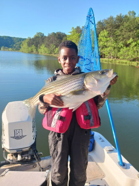 Un jeune garçon, âgé de 6, tenant un gros poisson dans ses bras sur un bateau.