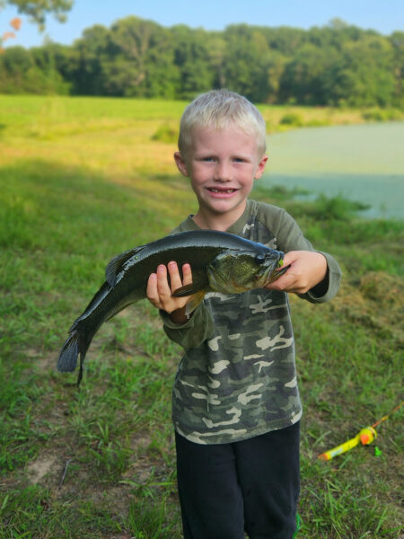 Un jeune garçon, âgé de 6, tenant un poisson noir de taille moyenne, souriant à l'appareil photo.