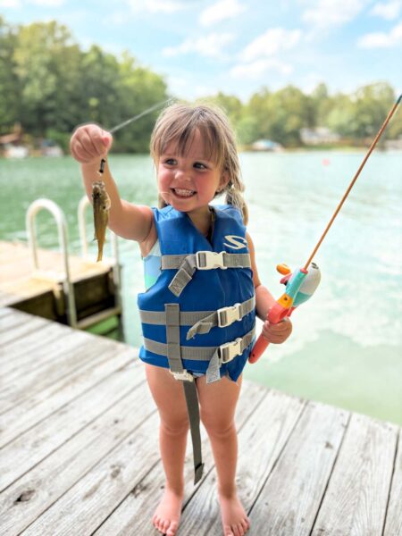 Une petite fille vêtue d'un gilet de sauvetage tient son poisson au bout d'une ficelle pour la caméra.