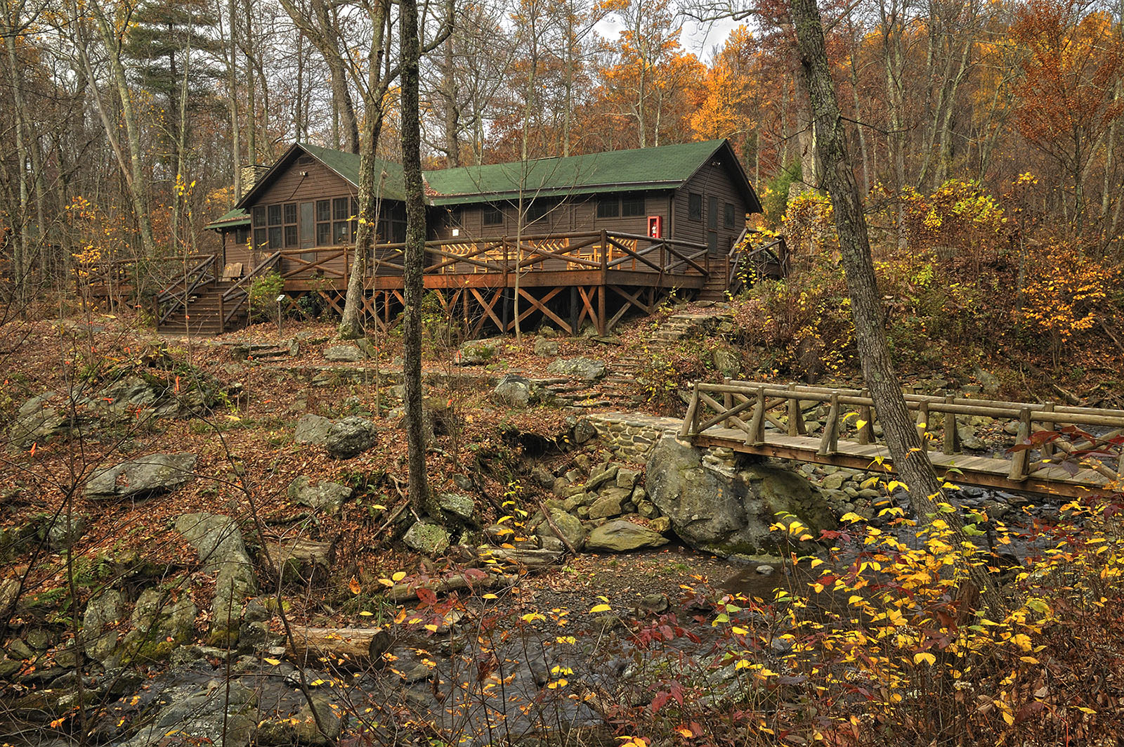 Photo couleur de la Brown House, une résidence en bois construite sur une pente rocheuse menant à une petite rivière. 