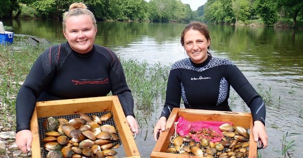 Deux femmes tenant des plateaux de moules lors du Musselrama devant une rivière