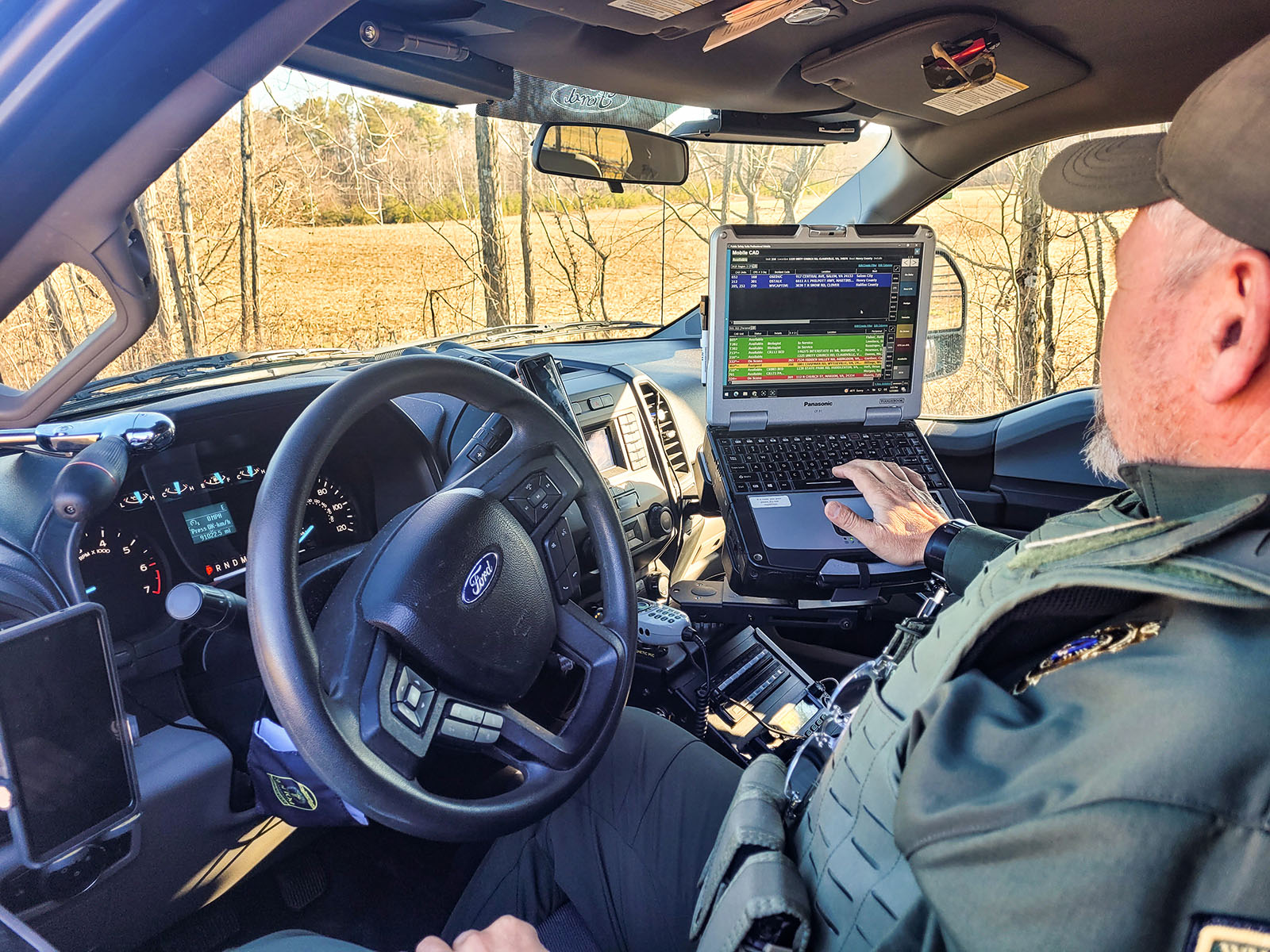 Photo d'un agent de la police de la conservation assis sur le siège du conducteur de son camion et regardant l'écran d'un ordinateur portable monté sur la console centrale.