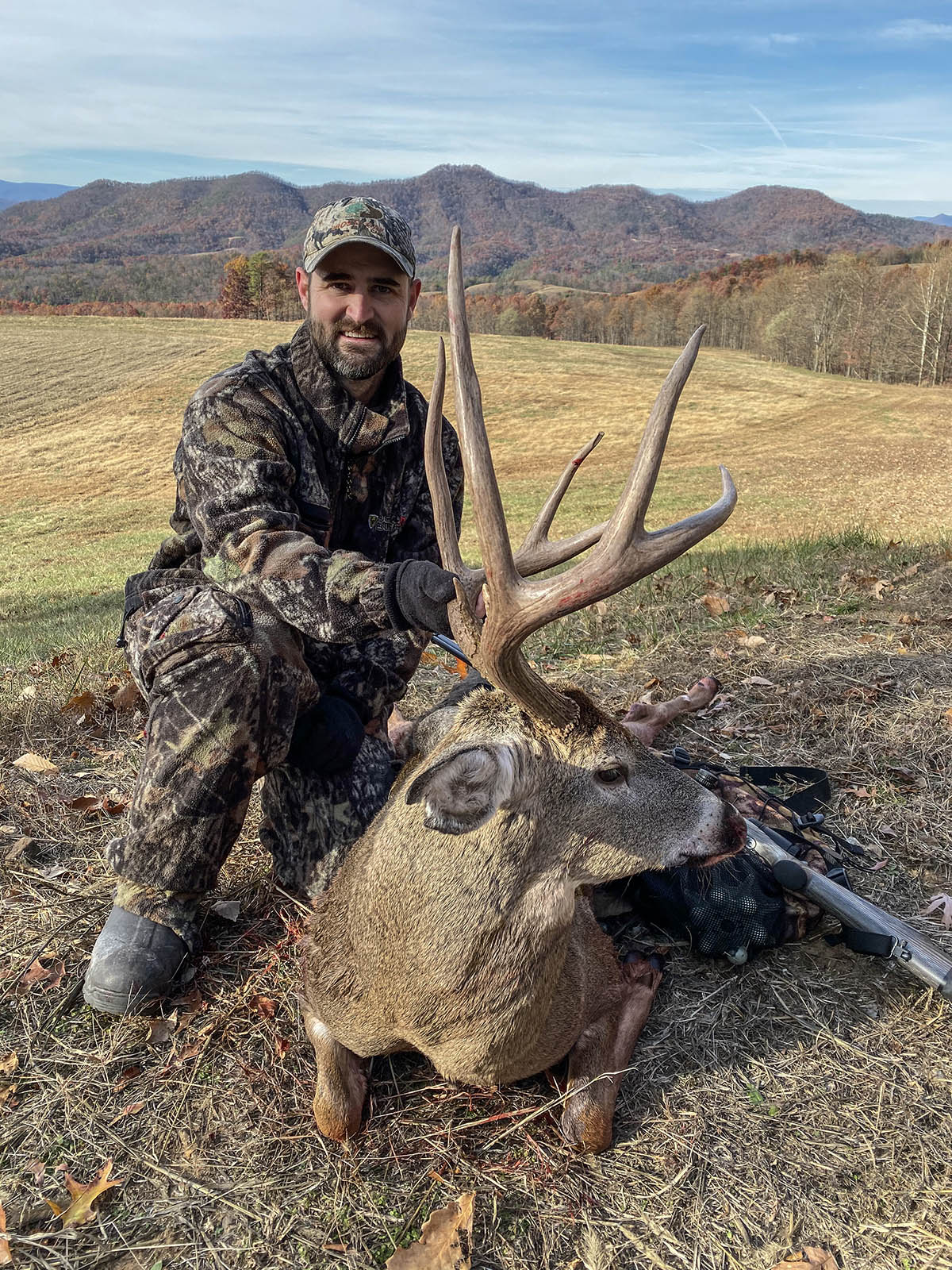 Chasseur en tenue de camouflage posant avec un grand cerf de Virginie aux larges bois.