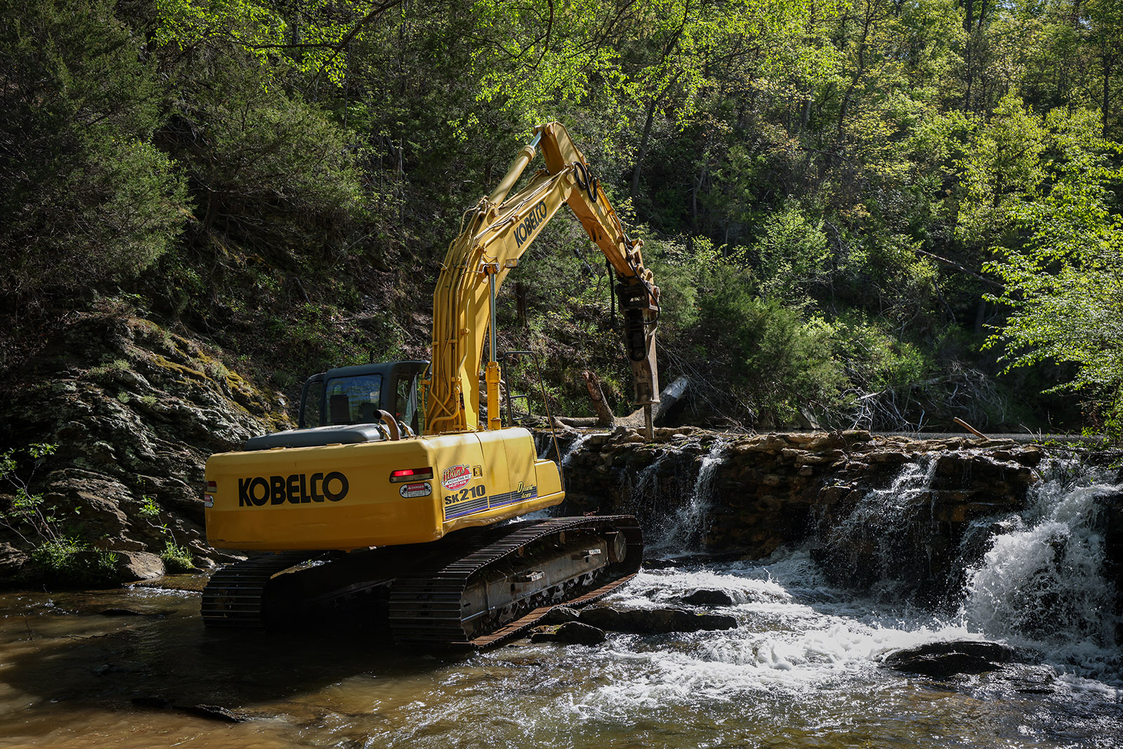 Photo d'une pelleteuse démolissant un vieux barrage sur une petite rivière.