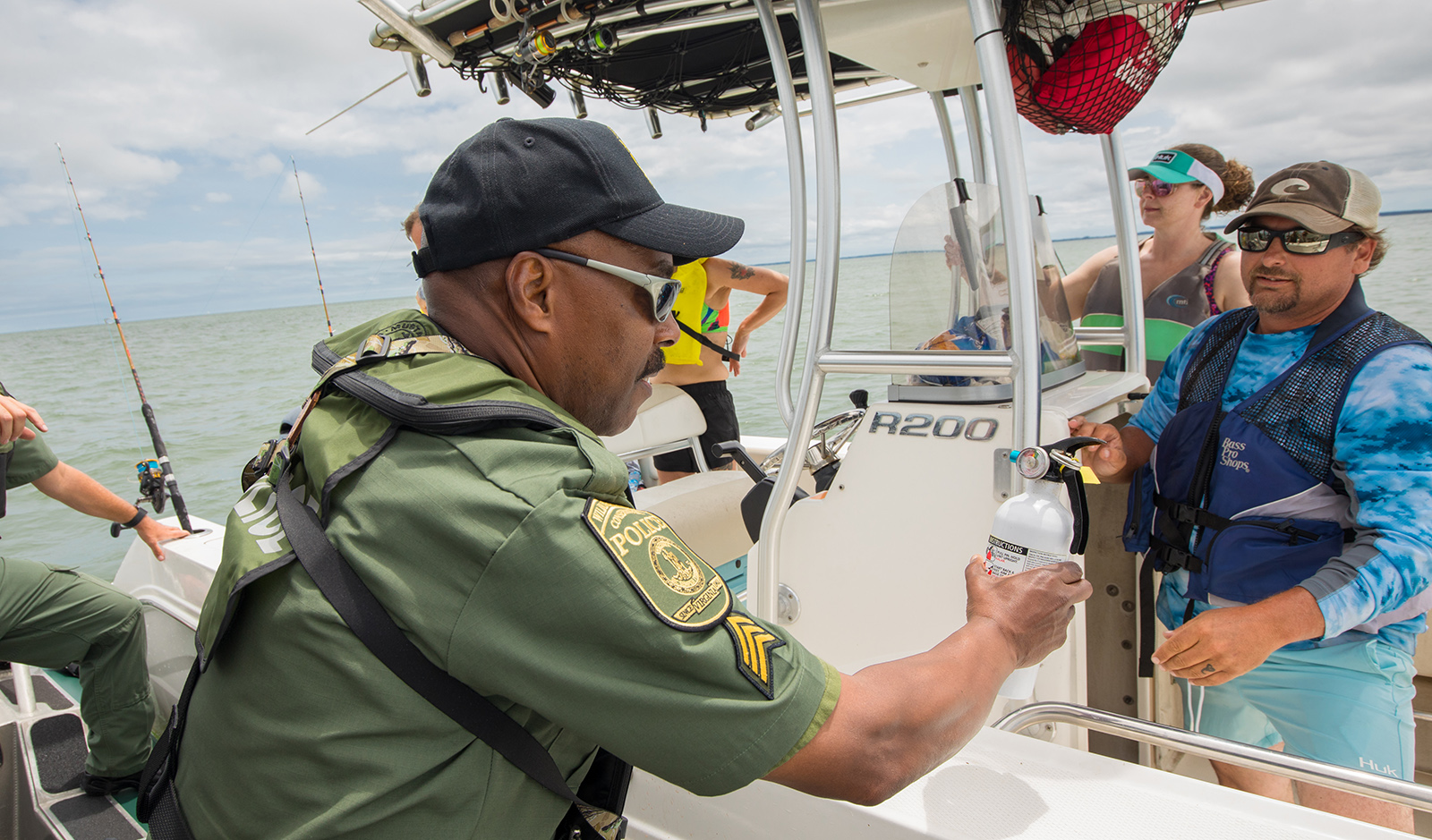 Photo d'un homme en uniforme sur un bateau, tenant un extincteur et s'adressant à deux personnes sur un bateau.