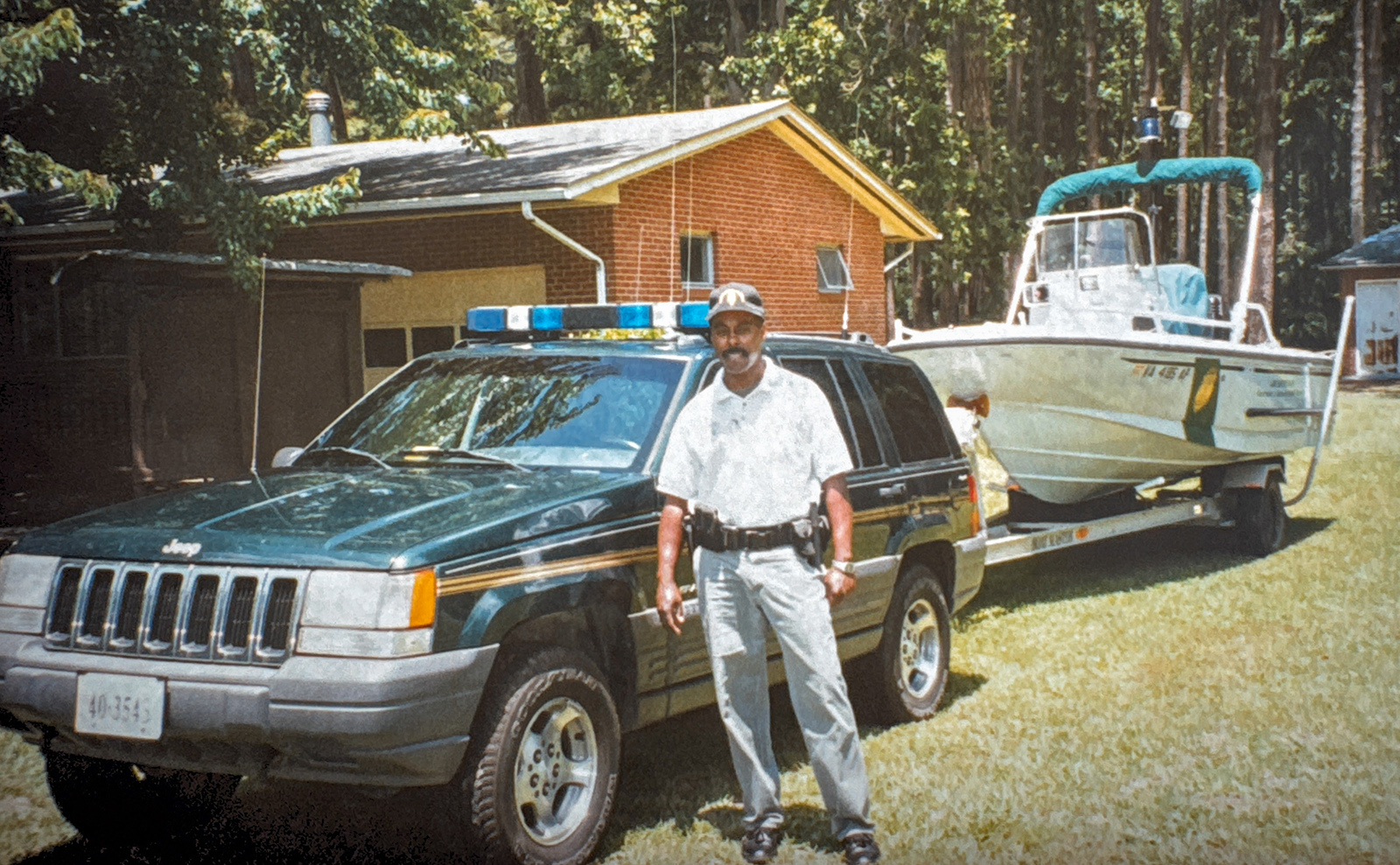Une photo d'un homme en uniforme avec une arme et un badge devant une Jeep accrochée à une remorque de bateau.