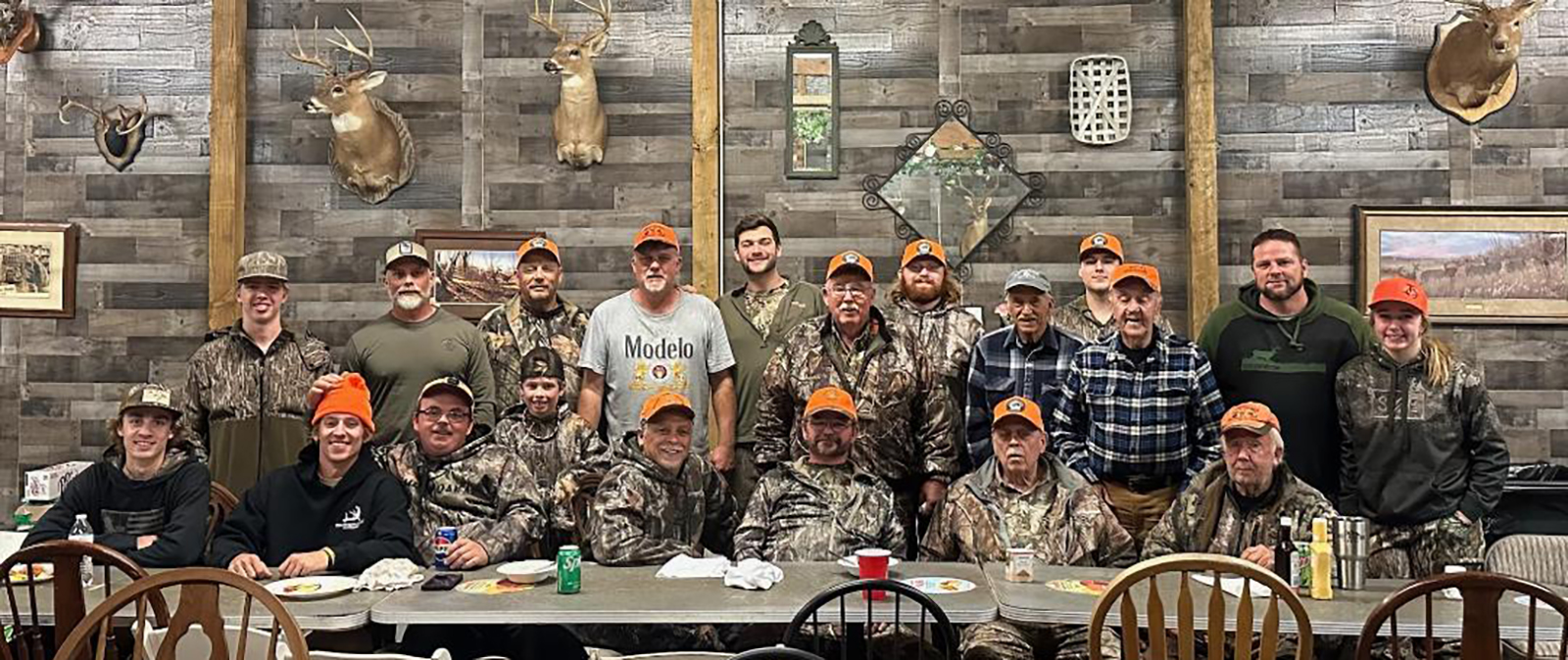 Une photo de 19 hommes tous habillés en tenue de camouflage, assis et debout derrière une longue table.