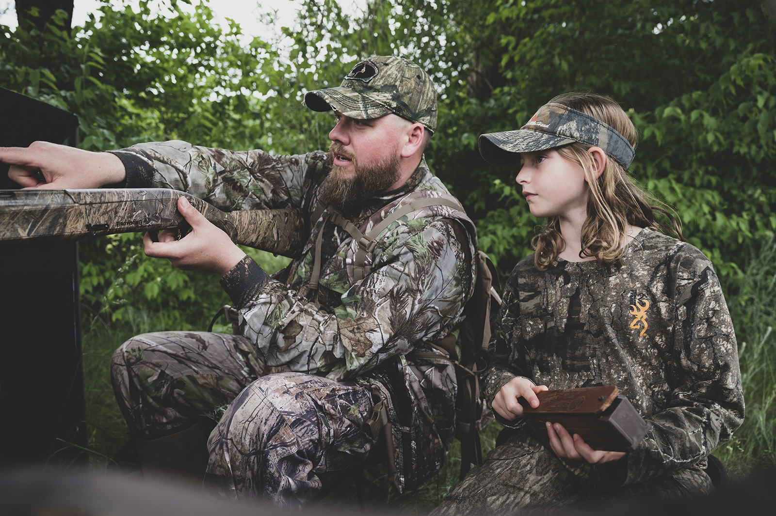 Photo d'un chasseur adulte tenant un fusil et pointant du doigt, tandis qu'une jeune chasseuse regarde et tient un appeau à dinde.