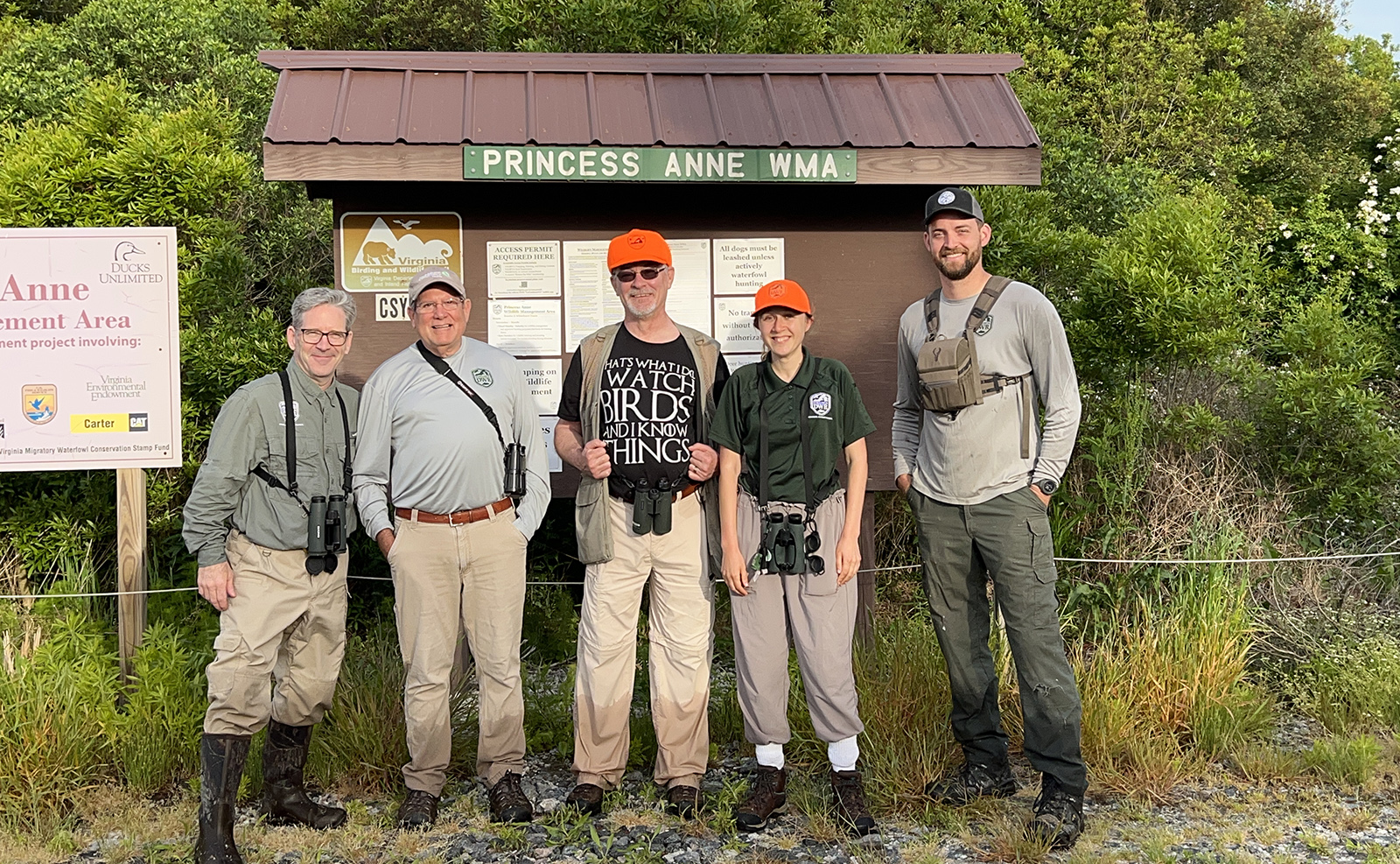 Un groupe de cinq personnes avec des jumelles posant devant un panneau étiqueté Princess Anne WMA.