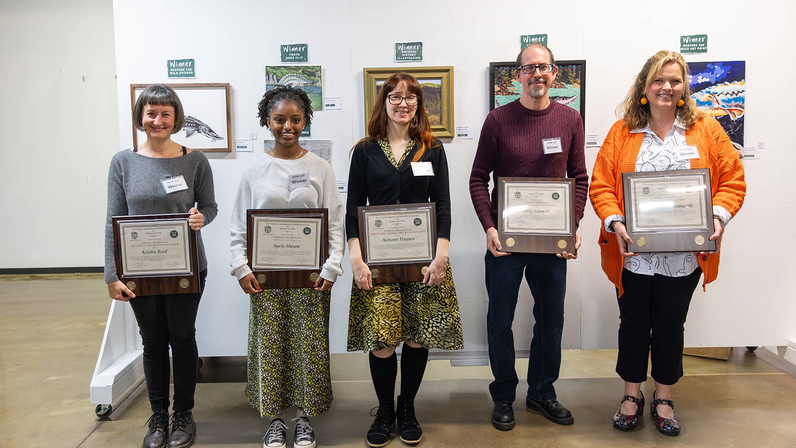 Une photo de cinq personnes debout tenant des certificats devant un mur orné d'œuvres d'art.