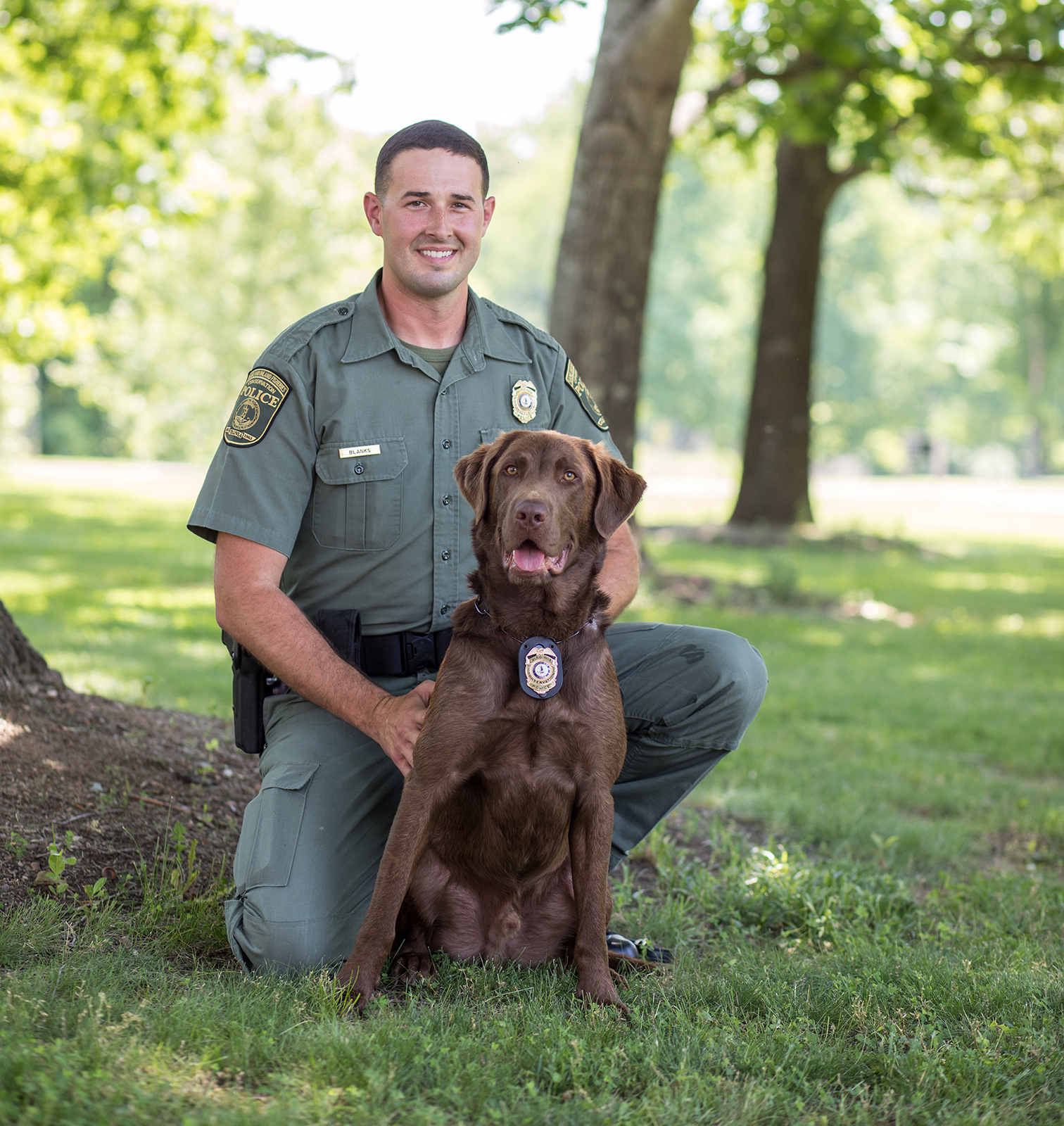 Une photo d'un homme en uniforme des forces de l'ordre agenouillé à côté d'un chien assis portant un badge sur son collier.
