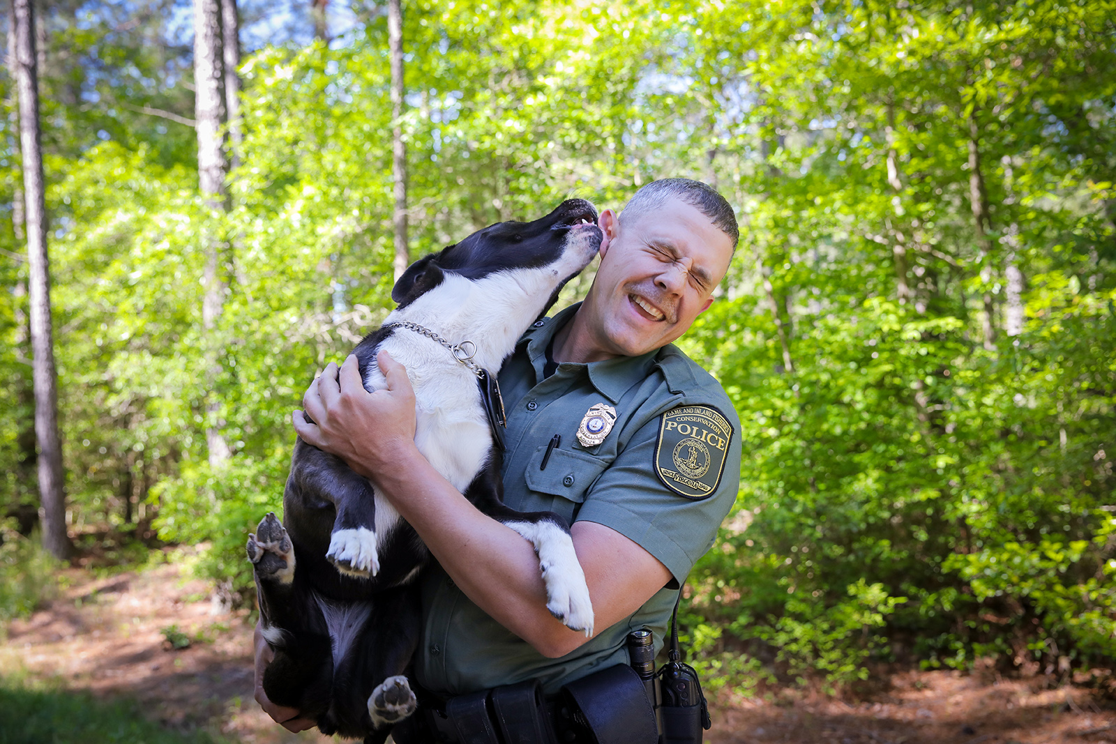 La photo d'un homme en uniforme des forces de l'ordre tenant un chien et souriant pendant que celui-ci lui lèche l'oreille.